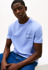 Jasnoniebieski bawełniany t-shirt z nadrukowanym logo na piersi, krótkimi rękawami oraz małym logo na rękawie. Do tego niebieskie dżinsy.