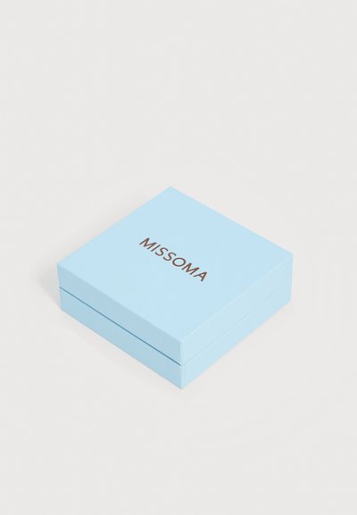 Φωτεινό γαλάζιο τετράγωνο κουτί κοσμημάτων με το λογότυπο «MISSOMA» σε χρυσό στο κέντρο του καπακιού, τοποθετημένο σε λευκή επιφάνεια.