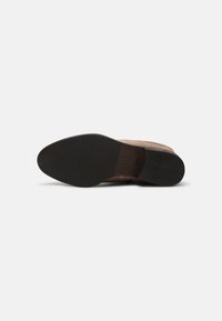 Semelle d’une chaussure en cuir marron avec un talon en caoutchouc noir et un caoutchouc noir texturé à l’avant sur un fond blanc uni.