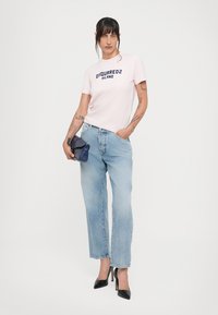 Pink cotton t-shirt with “DSQUARED2 MILANO” print, light blue straight-leg jeans, and black high-heeled shoes. Blue clutch with pattern.