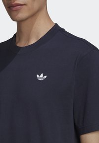 Mörkblå bomullströja med korta ärmar och rundad halsringning. Har en liten vit broderad Adidas-logga på vänster bröst.