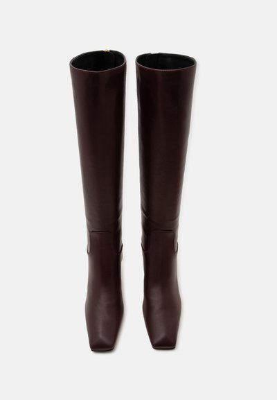 Bottes hautes en cuir brun foncé avec des bouts carrés, debout contre un fond blanc uni.