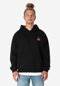 Schwarzer Baumwoll-Hoodie mit einer Fronttasche, Kordelzugkapuze und einem kleinen gestickten Design einer Pflanze in einem Topf. Weicher Stoff.