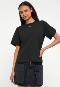 Melnas kokvilnas T-krekls ar īsām piedurknēm, apaļu kakla izgriezumu un nelielu logotipa detaļu uz krūtīm, kombinēts ar melnu džinsa svārku ar kabatām.