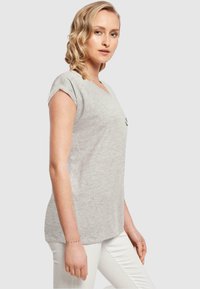 Graues V-Ausschnitt-T-Shirt aus weichem Stoff mit kurzen, umgeschlagenen Ärmeln, mit einem dezenten Logodetail auf der Brust, kombiniert mit weißen Hosen.
