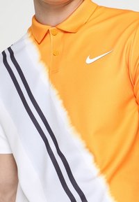 Gros plan d'une personne portant un polo Nike orange et blanc avec des rayures diagonales noires et deux boutons orange.