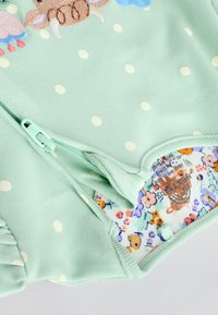 Menta zöld baba body fehér pöttyökkel, részleges cipzárral, hímzett zsiráf mintával és virágmintás bélés belső oldalán.