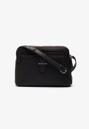 Sac besace noir en tissage avec sangle en cuir réglable, boucle dorée et fermeture éclair sur le dessus sur fond blanc.
