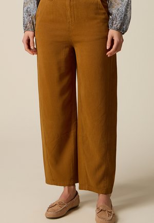 Szerokie spodnie w kolorze rdzy noszone z beżowymi mokasynami i kwiecistą, długorękawową bluzką, krótką na wysokości talii i kostek.