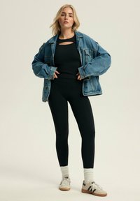 Czarny sportowy top z wycięciem, oversize'owa dżinsowa kurtka, czarne legginsy oraz białe skarpetki w butach z czarnymi paskami.