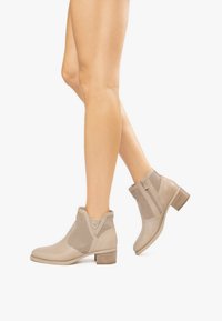 Bottines beige avec un devant en cuir lisse et des panneaux en maille. Elles présentent un talon empilé, une fermeture éclair latérale et des coutures décoratives.