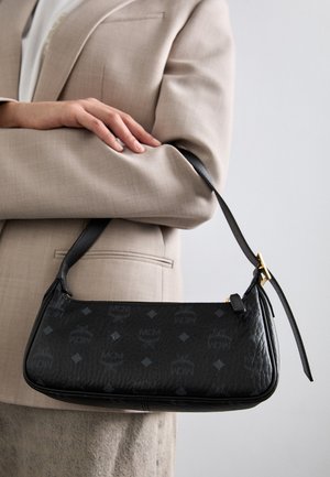 Schwarzlederne Handtasche mit dem eingeprägten MCM-Logo-Muster, rechteckiger Form, schlankt Handgriff und Akzenten aus goldfarbener Hardware.