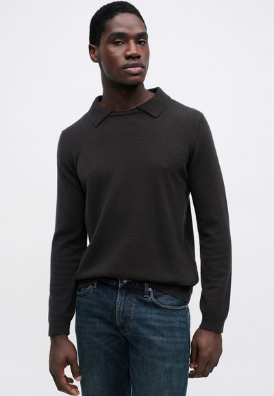 Ciemnoszary sweter z długim rękawem i kołnierzykiem, o miękkiej fakturze, noszony z niebieskimi dżinsami.