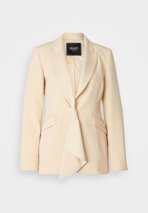 Pale beige blazer with a satin lapel, tie detail, and two flap pockets, featuring a smooth, tailored finish and structured shoulders.