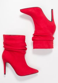 Botines de ante rojo con tacón, diseño arrugado, puntera afilada y alto tacón de aguja. Textura suave y color vibrante en todo.