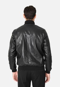 Giacca bomber in pelle nera con colletto e polsini a costine, caratterizzata da una texture liscia e una vestibilità leggermente ampia all'orlo.