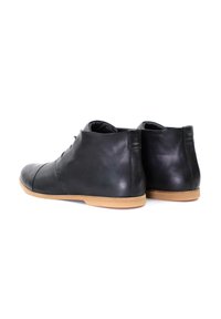 Botas de cuero negro a la altura del tobillo con punta redondeada, que presentan un acabado liso y una suela de goma marrón. Tacón ligero y detalles de costura mínimos.