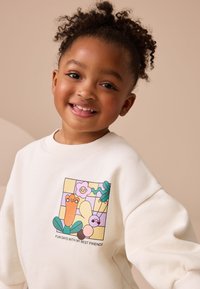 Cream-colored sweatshirt with a graphic featuring cartoon characters, flowers, and leaves. Ribbed neckline and cuffs for fit.