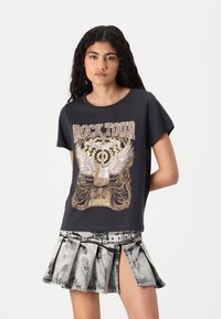 T-shirt noir à manches courtes avec un imprimé graphique d'une guitare et d'ailes, associé à une jupe en denim gris plissée avec une fente sur le côté.