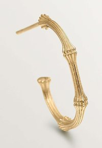 Pendientes de aro en tono dorado que presentan un diseño texturizado y estriado, formados con una estructura curva y acentuados con extremos ensanchados.
