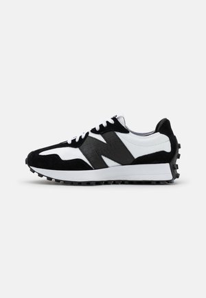 Baskets athlétiques noires et blanches avec un logo "N" noir texturé, des lacets blancs et une semelle à crampons, vues de côté sur un fond uni.