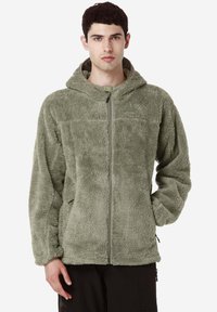 Giacca in pile verde con zip frontale, cappuccio e tasche laterali. Tessuto morbido e vestibilità rilassata, con logo sul petto.