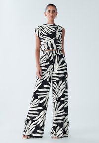 Melnā un baltā lapu raksta košu komplekts, kas sastāv no īsas augšdaļas ar kapuci un augsto vidukli platiem biksēm ar elastīgu jostu.