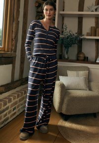 Set de loungewear cu dungi bleumarin și corai, format dintr-o bluză cu mâneci lungi și nasturi și pantaloni evazați, realizat dintr-un material moale, asortat cu papuci ușori.