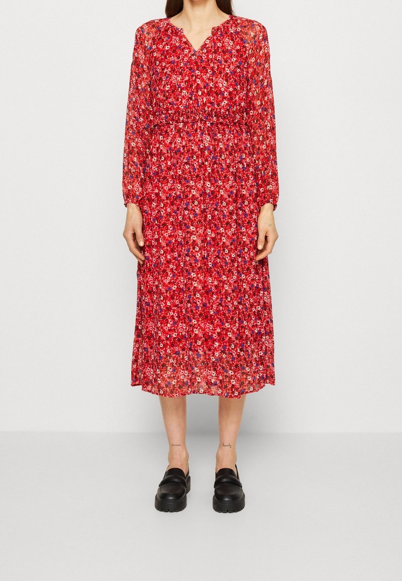 Robe midi rouge à motifs floraux avec manches longues en tissu transparent et taille froncée. Portée avec des chaussures noires épaisses.