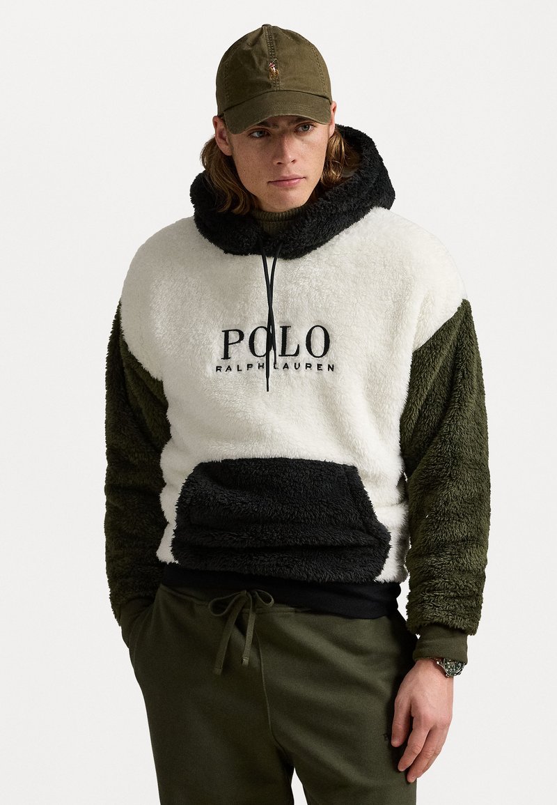 Haut à capuche en polaire blanc et vert olive avec des accents noirs, poche kangourou et logo "Polo Ralph Lauren". Associé avec un pantalon de jogging olive et une casquette.