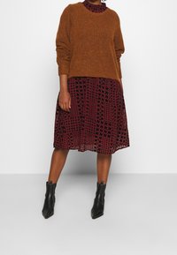 Brun stickad tröja över en svart klänning med ett rött blommönster. Kombinerad med svarta ankelstövlar med spetsiga tår.