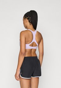 Sujetador deportivo lavanda con diseño de espalda de nadador y detalle recortado, acompañado de pantalones cortos negros con ribete blanco y cintura elástica.