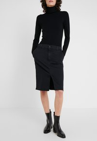 Jupe en denim noir avec une fente sur le devant, de longueur mi-longue, dotée de poches et d'une fermeture à boutons. Associée à un col roulé noir à manches longues et à des bottines.