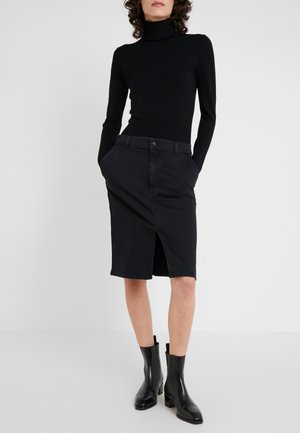 Jupe en denim noir avec une fente sur le devant, de longueur mi-longue, dotée de poches et d'une fermeture à boutons. Associée à un col roulé noir à manches longues et à des bottines.