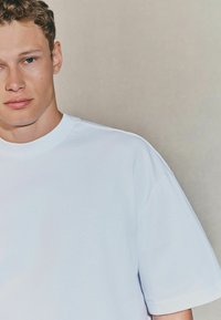 Camiseta de algodón blanca con cuello redondo, mangas cortas y un corte relajado. Textura suave, diseño minimalista, sin patrones ni acentos.