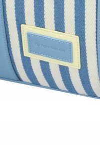 Blauwe en crème gestreepte stoffen tas met een gladde blauwe nepleer afwerking. Voorzien van een rechthoekig lichtgeel etiket met "TOM TAILOR" in reliëf.