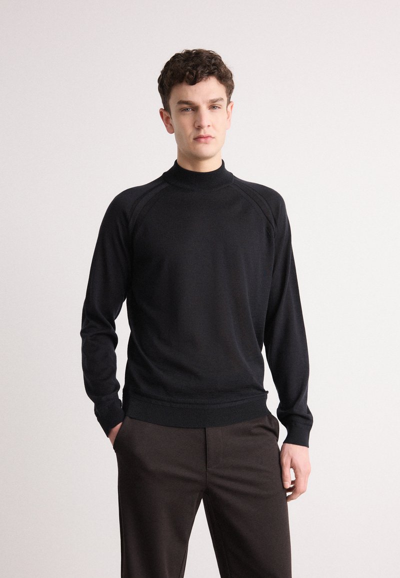 Schwarzer Strickrollkragenpullover mit langen Ärmeln, gerippten Bündchen und Saum; verfügt über eine glatte Textur und ein athletisches Raglan-Design.