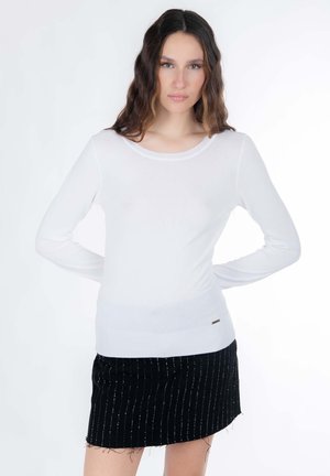 Haut blanc à manches longues de coupe ajustée avec un col bateau, associé à une jupe noire ornée de rayures verticales argentées et d'un ourlet effiloché.