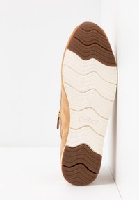 Botte en daim beige avec une semelle extérieure en caoutchouc marron texturée présentant un motif ondulé et une semelle intermédiaire de couleur crème. Détail zippé sur le côté.