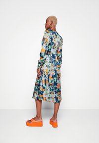 Vestido de manga longa com um padrão abstrato multicolorido em azul, verde, laranja e roxo; combinado com sandálias de plataforma laranja.