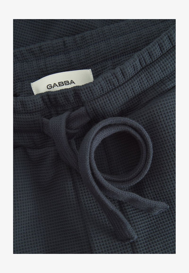 Tumedat merevärvi tekstuuriga vabaajajalanõud, millel on kootud vöökoht, nöör ja silt, millel kiri "GABBA" tikitud märgil.