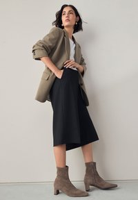 Knee-length black skirt paired with a beige blazer, white t-shirt, and taupe suede ankle boots featuring a zipper and block heel.
