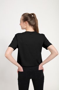 Sort bomulds T-shirt med korte ærmer, rund halsudskæring og en afslappet pasform, båret med mørke jeans. Modellen har håret bundet tilbage.