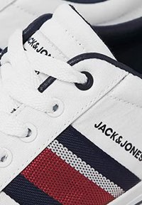 Baskets en toile blanches avec des accents bleu marine, des détails rayés rouge et bleu marine, et des lacets blancs ; logo imprimé sur le côté. Œillets ronds pour les lacets.