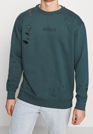 Sweatshirt teal avec des détails décolorés et usés, y compris des déchirures et des trous, et un logo noir "MENNACE" sur le devant ; poignets et ourlet côtelés.