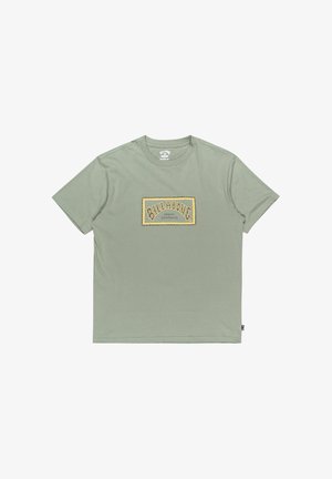 Lysegrøn bomuldst-shirt med en rektangulær gul grafikprint, der viser "BILLABONG" og "AUSTRALIA" i en stiliseret skrifttype. Korte ærmer.