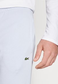 Világoskék tréningnadrág, puha textúrával, rugalmas derékkal, és hímzett zöld krokodil logóval a bal oldalon.