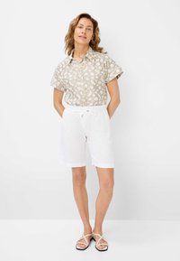 Blusa di lino chiaro con motivo floreale, chiusura a bottoni, maniche corte; abbinata a pantaloni corti bianchi con coulisse e sandali nudi con cinturini.