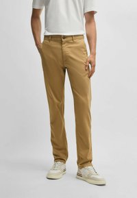 Beige chinos made from cotton blend, featuring a straight cut, button and zip closure, and side pockets, paired with white sneakers.