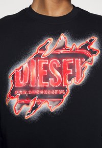 Sudadera negra con un gran diseño gráfico en rojo y blanco, que representa la palabra "DIESEL" con un efecto texturizado de spray.